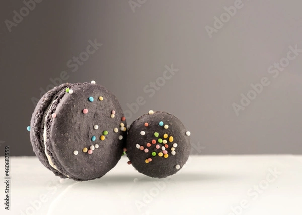 Obraz Purple cute french macarons with decorative colorful candies and white cream. Shot isolated against white and gray background