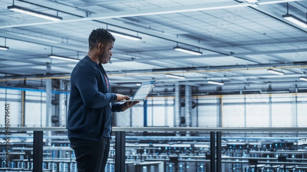Fototapeta Data Center Engineer Using Laptop Computer. Server Farm Cloud Computing Specialist Facility with Black Male System Administrator Working with Data Protection Network for Cyber Security.