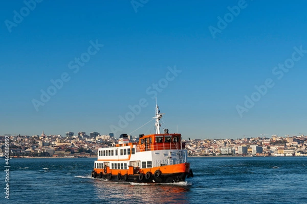 Fototapeta A traditional cacilheiro ferry boat crossing the Tagus River (Rio Tejo) with the city of Lisbon skyline on the background.