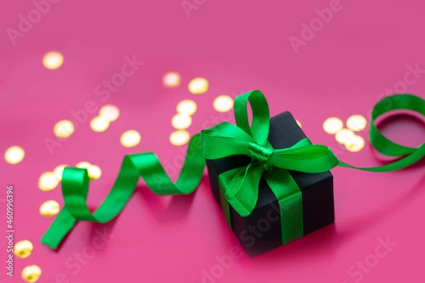 Fototapeta Gift box with green ribbon bow on light pink background with gold confetti. Festive decor background. Top view.