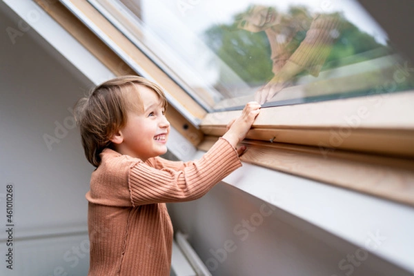 Obraz Close up portrait of a little preschool boy looking at the window and laughing. Happy smiling child spends time at home alone.