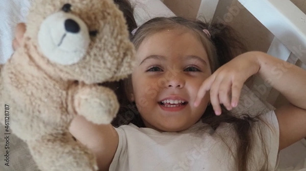 Fototapeta little cute girl is going to go to bed. indulges in, does not want to sleep. naughty. Cute little girl sleeping with teddy bear in bed