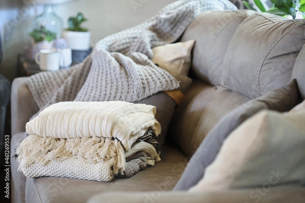 Fototapeta Stack of a variety of soft knit throw blankets stacked on a grey couch in a farmhouse style living room. Selective focus on covers with blurred foreground and background.