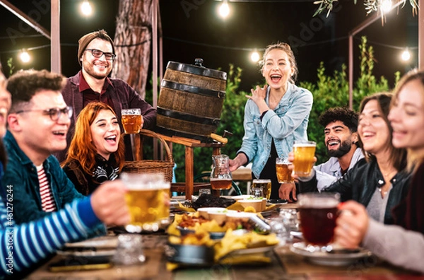 Obraz Happy men and women having fun drinking out at beer garden - Social gathering life style concept on young people enjoying hangout time together at night - Warm filter with shallow depth of field