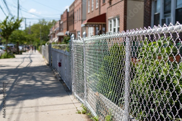 Fototapeta Chain Link Fence along an Empty Sidewalk with a Row of Old Homes in Astoria Queens New York