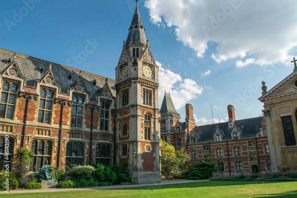 Fototapeta Historical bricked building attached to a medieval style clock tower in front of lawn and benches in Cambridge England