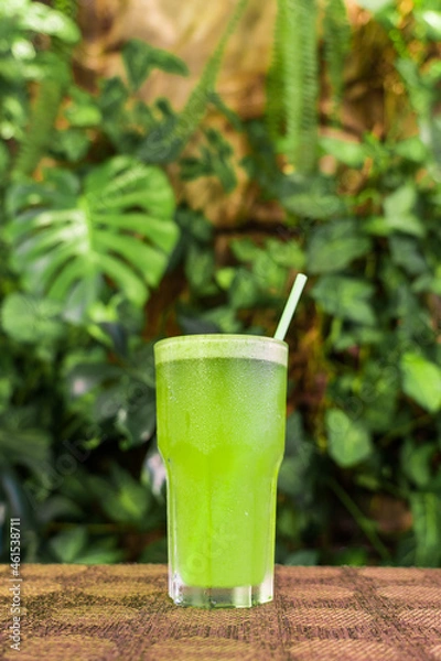 Fototapeta Delicious smoothie of natural vegetables and fruits on an unfocused background of leaves. Healthy fitness diet concept