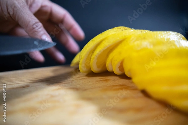 Fototapeta Hands slicing orange above wooden surface with black background