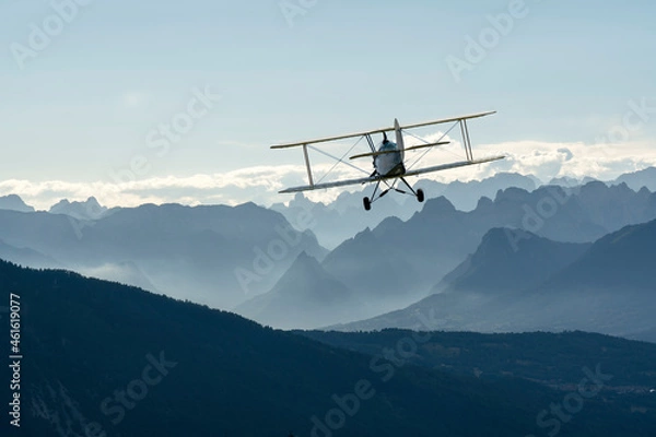 Fototapeta biplane plane flies over the mountains at sunset