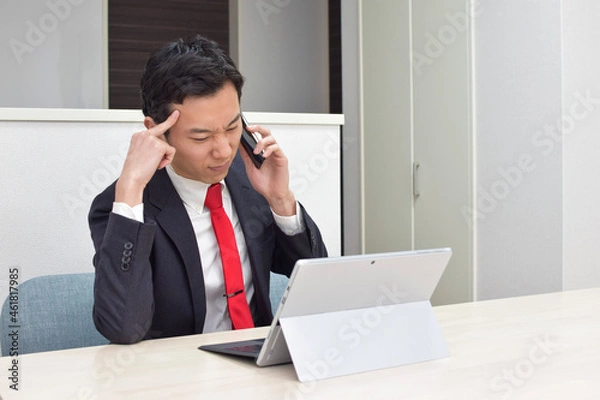 Obraz A young Asian man during telework at home talks on his phone and thinks about how to answer to his client