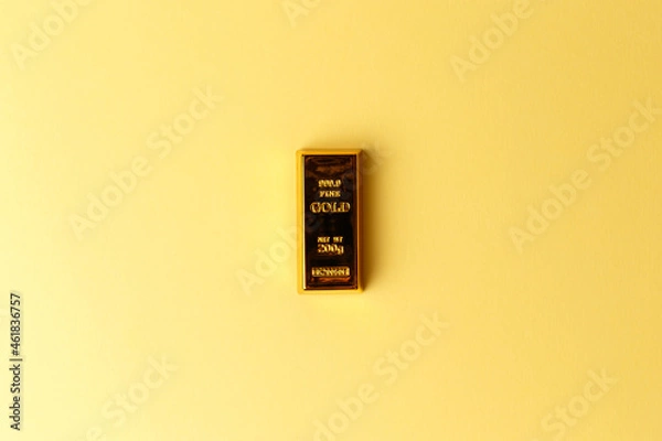Obraz A gold bar on a yellow background. Financial concept. Flat lay. Top view. The concept of a gold reserve. A protective financial asset. The stock market. Golden ETF