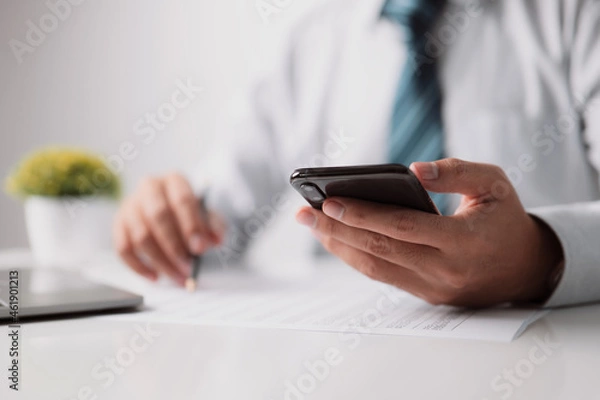 Fototapeta Man editor is reading a document or report at work, while a financier is reading a contract agreement on paper and reviewing the newest financial news on a smartphone application.