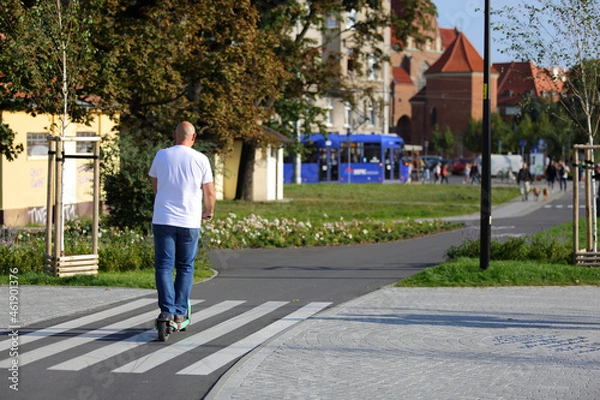 Obraz Dojżały mężczyzna jedzie na hulajnodze elektrycznej po ścieżce rowerowej.