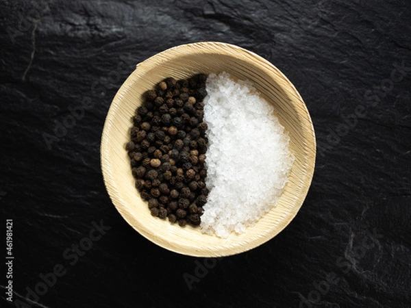 Obraz Coarse sea salt and whole black peppercorns in bamboo bowl on slate worktop, background. Flat lay, top view.