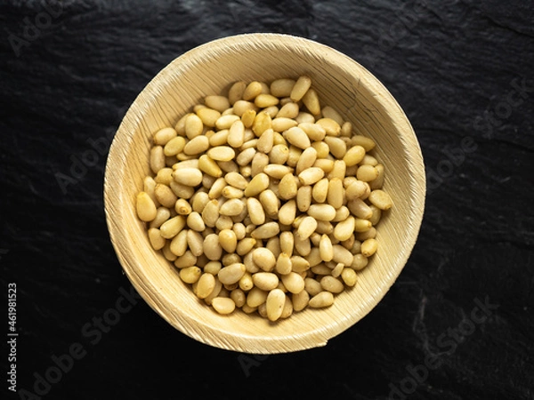 Obraz Pine nuts in a bamboo bowl on slate worktop, background. Flat lay, top view.