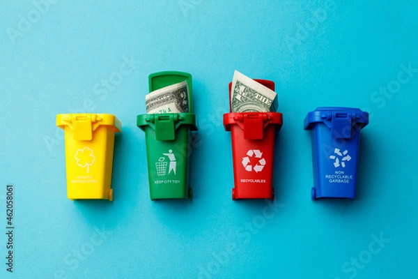Fototapeta The concept of the collapse of the dollar. Wasted money is the same as being thrown in the trash. Trash cans of different colors with the recycle logo with discarded money on a turquoise background