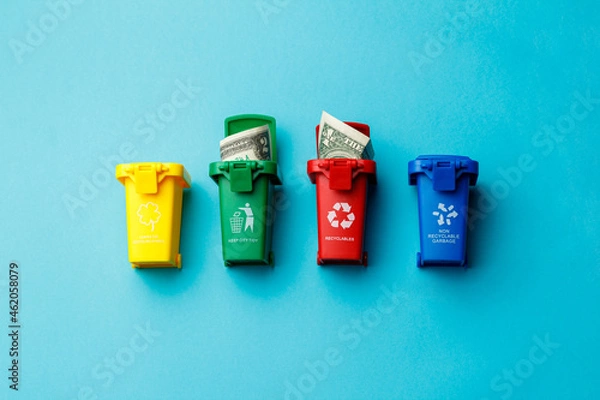 Fototapeta The concept of the collapse of the dollar. Wasted money is the same as being thrown in the trash. Trash cans of different colors with the recycle logo with discarded money on a turquoise background