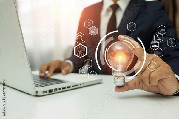 Fototapeta Business man holding light bulb on the Green background nature and writing on note book it for financial