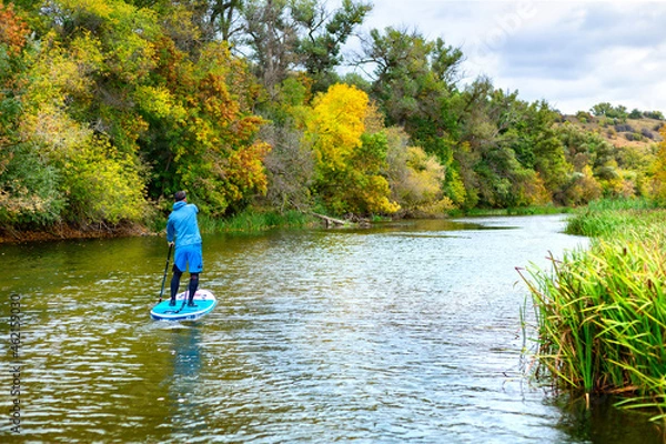 Fototapeta A man on a SUP swims along the river in autumn in cloudy weather