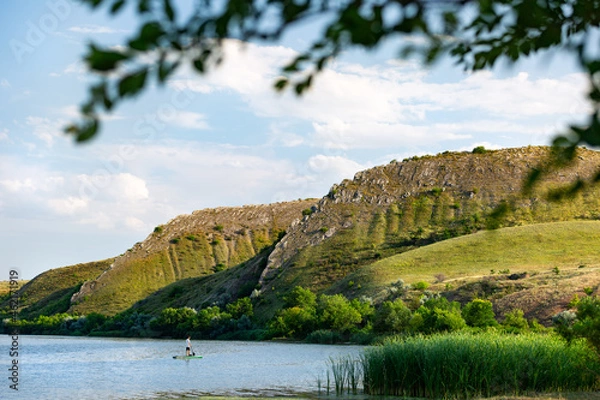 Fototapeta 
A man on a SUP on the river in summer at sunset against the background of mountains Two sisters