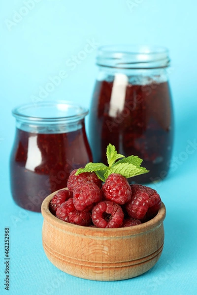 Fototapeta Jars of raspberry jam with ingredients on blue background