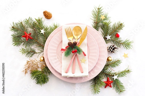 Obraz concept of christmas table setting. two pink plates and pink and gold cutlery with decor on a linen napkin. fir branches, cones, balls and stars..