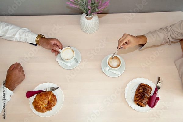Obraz Desayuno. Hombre y mujer desayunando en cafetería. Cafés y bollos. Bollería sobre mesa de madera. Desayuno de trabajadores.