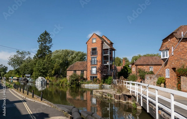 Obraz Newbury, Berkshire, England, UK. 2021.  White wooden swing bridge over the Kennet and Avon Canal at Newbury, tall buildings a former granary. UK