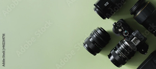 Fototapeta Photographer's or videographer equipment, composition of a camera and lenses on a green background, flat lay. Mock up with space for text, top view. Banner format.