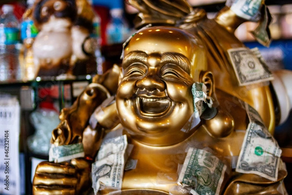 Fototapeta Bronze Buddha statue with Dollar Bills taped to it 
