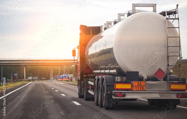Fototapeta A truck with a tank trailer transports a liquid dangerous cargo on a highway against the backdrop of a sunset. Copy space for text