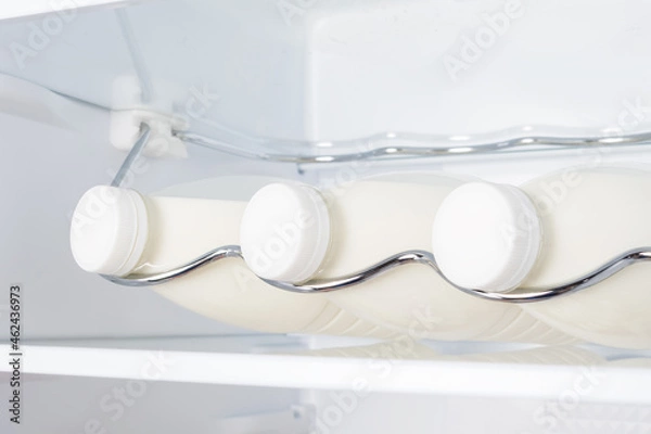 Fototapeta three bottles of farm milk on a shelf in the refrigerator, close-up