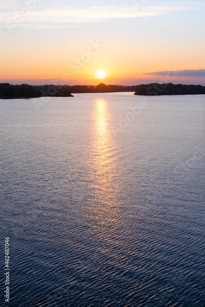 Obraz Bright colorful sunset over the Daugava river. The sun sets low above the horizon in a beautiful cloud, and is reflected on the surface of the water. Natural landscape
