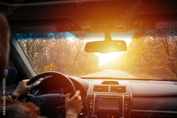Fototapeta man driving a car on an autumn road at sunset. Close-up of hands on a steering wheel. view from the driver's back. empty road. view from the car