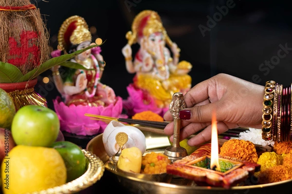 Fototapeta Hands Of Girl Holding Ghanti Bell. Clay Diya Deep Dia Lamp Illuminated In Pooja Thali For Aarti Of Maa Lakshmi & Bhagwan Ganesh Deva. Diwali Puja , New Year, Deepawali Or Shubh Deepavali Theme