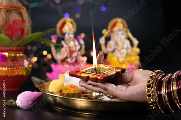 Fototapeta Hands Of Girl Holding Illuminated Clay Diya Deep Dia Lamp With Pooja Thali, Flowers And Doing Aarti Of Maa Lakshmi & Bhagwan Ganesh Deva. Diwali Puja , New Year, Deepawali Or Shubh Deepavali Theme