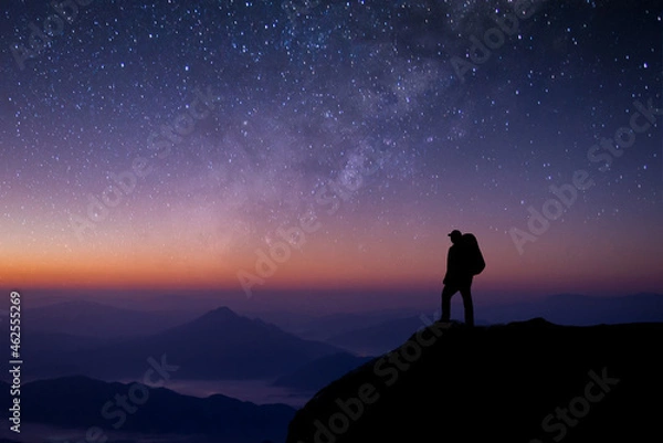Fototapeta A young tourist with a bag is standing looking at the stars. The Milky Way and the beauty of the night sky alone on the top of the mountain. He felt successful at reaching his intended destination.