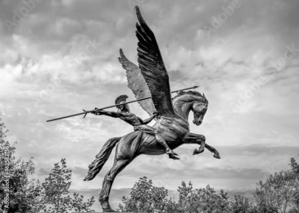 Obraz Bellerophon riding winged horse pegasus spear in hand dark sky moody, trees black and white