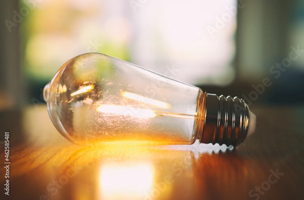 Fototapeta Close up of light bulb on wooden table. energy concept or invention