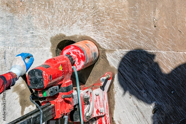 Fototapeta Worker is drilling to concrete wall with core drill machine in the construction site. A modern core drill is a drill specifically designed to remove a cylinder of material, much like a hole saw.