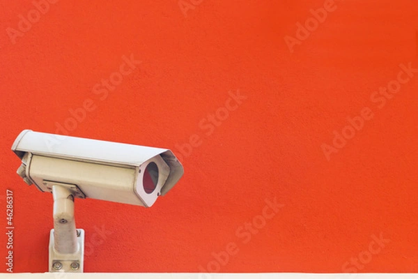 Fototapeta Security camera on a red wall background.