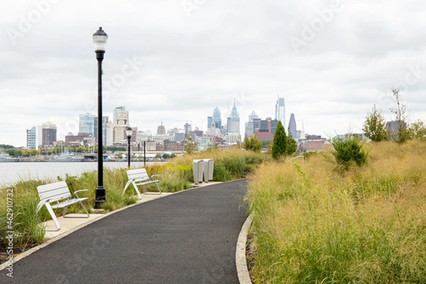 Fototapeta Walking path through the plants and grasses growing at RCA Pier Park on the Camden Waterfront, New Jersey, USA, with the Philadelphia skyline in the distance