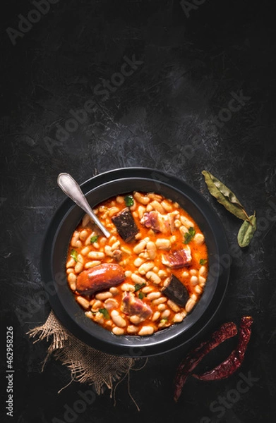 Fototapeta Traditional recipe of beans with chorizo and blood sausage called “Fabada Asturiana” on a dark table with some ingredients around. Typical Spanish food with “compango”. 