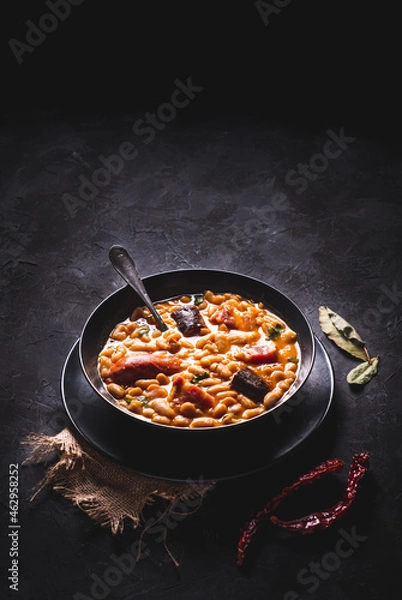 Fototapeta Traditional recipe of beans with chorizo and blood sausage called “Fabada Asturiana” on a dark table with some ingredients around. Typical Spanish food with “compango”. 
