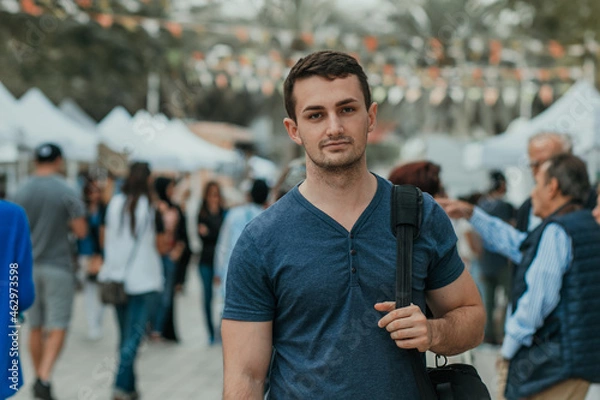 Fototapeta Handsome looking guy, international student male looking at the camera with a backpack and crowd people background 