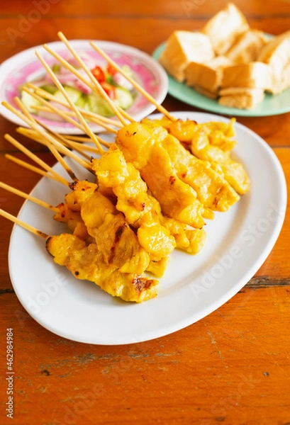Fototapeta Closed up street food it's grill pork satay or grilled pork on white dish served with bean sauce and pickle cucumbers and onions in vinegar.