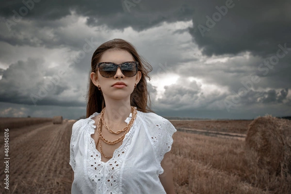 Obraz a woman in big glasses and a white blouse in an autumn field dramatic sky in clouds