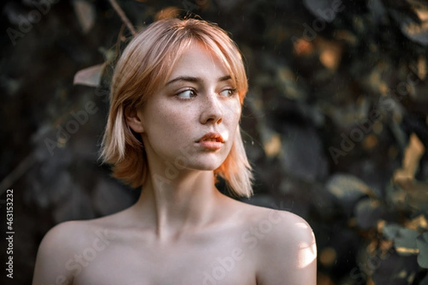 Obraz a young blonde without clothes looks towards a portrait in a park against a background of foliage