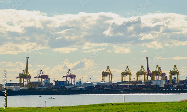 Fototapeta Port Botany  with shipping containers and container cranes against a cloudy sky. Port Botany, Sydney, New South Wales, Australia.