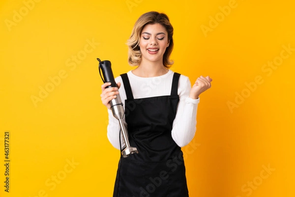 Fototapeta Girl using hand blender isolated on yellow background celebrating a victory in winner position